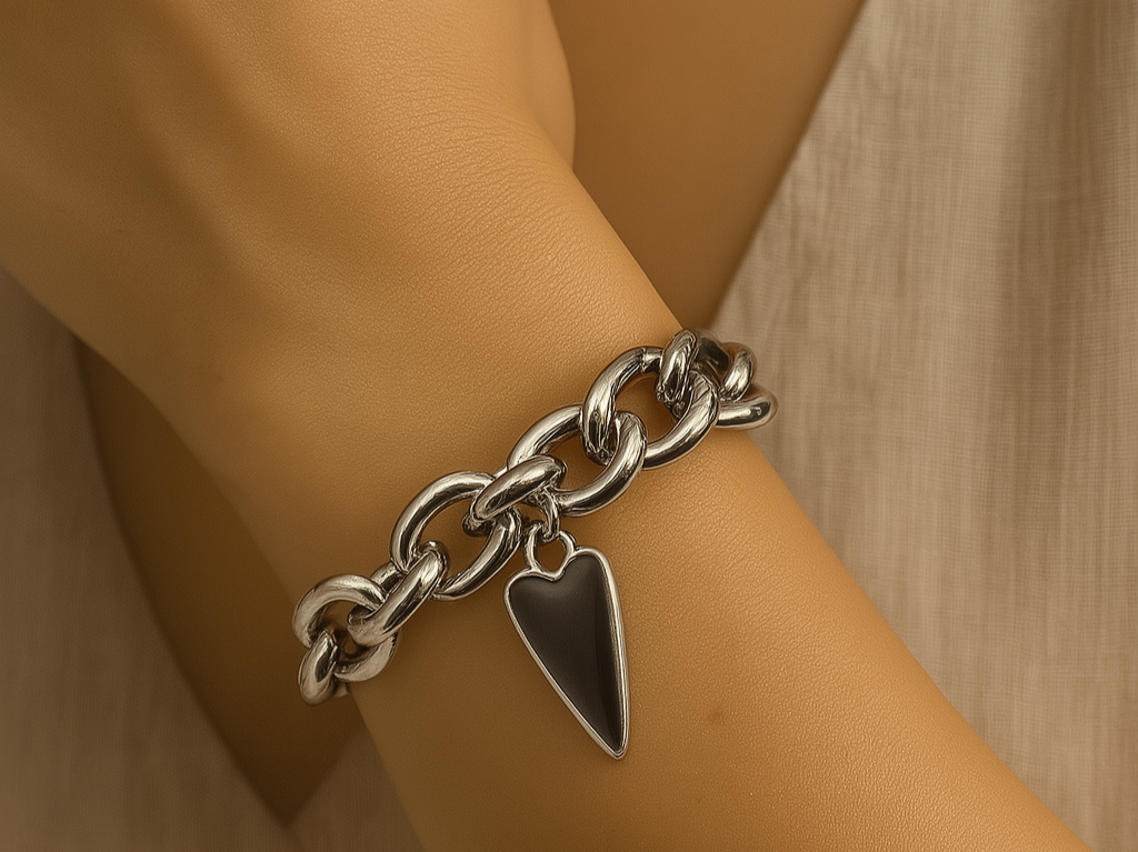 Silver chain bracelet with a heart charm on a wrist against a neutral background
