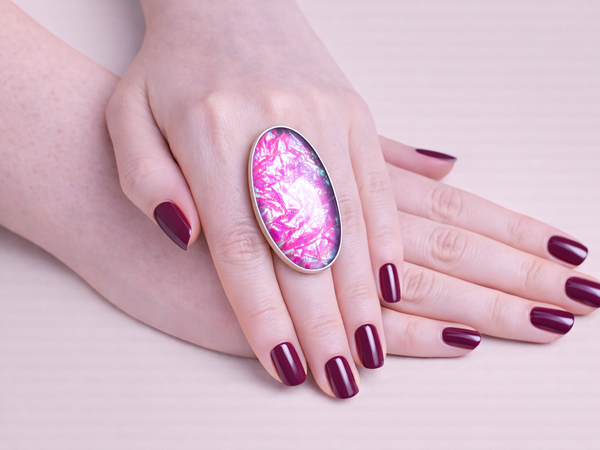 Hand wearing a ring with a pink and purple gemstone on a light background