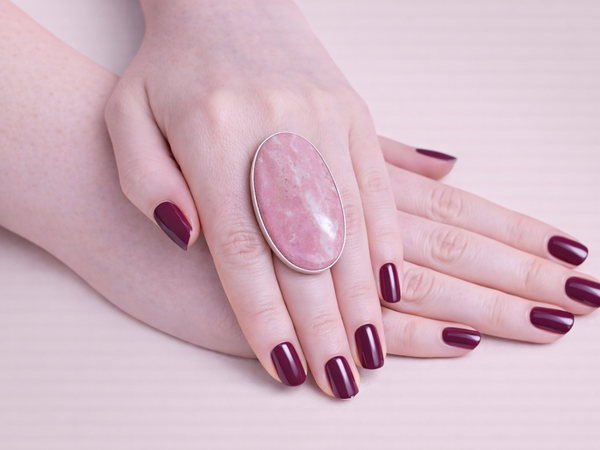 Hand wearing a pink ring with a stone on a light background