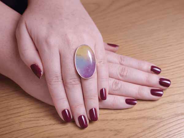 A bold yet not so big solar quartz ring featuring a soft blend of pastel tones, being worn on a models hand