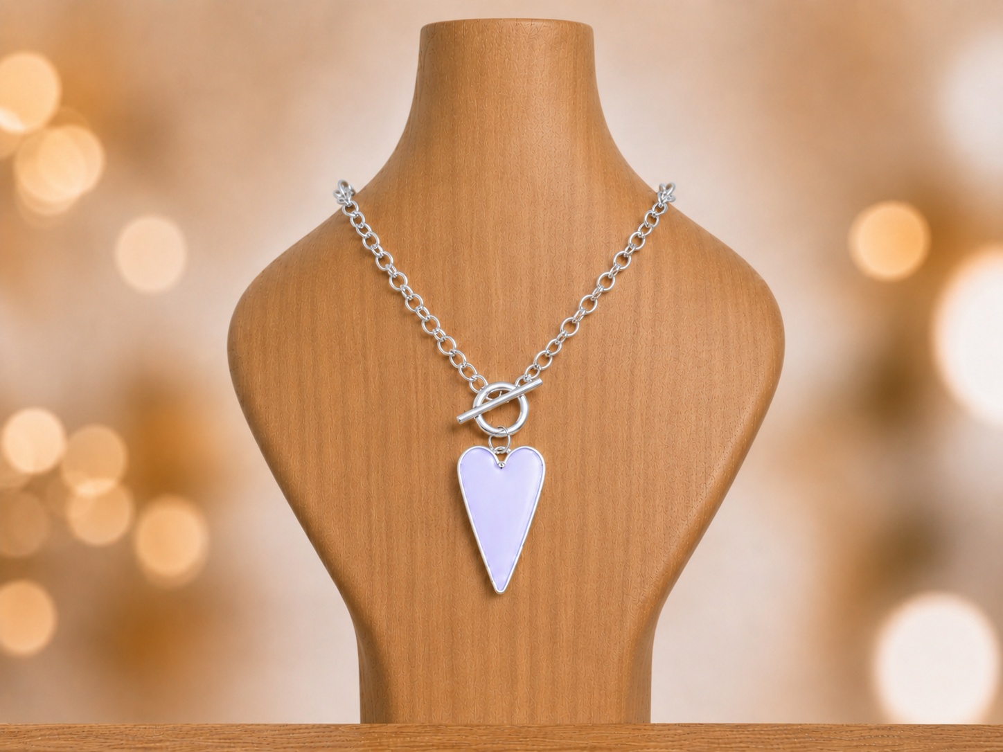 Silver necklace with a heart-shaped pendant on a wooden mannequin against a blurred background