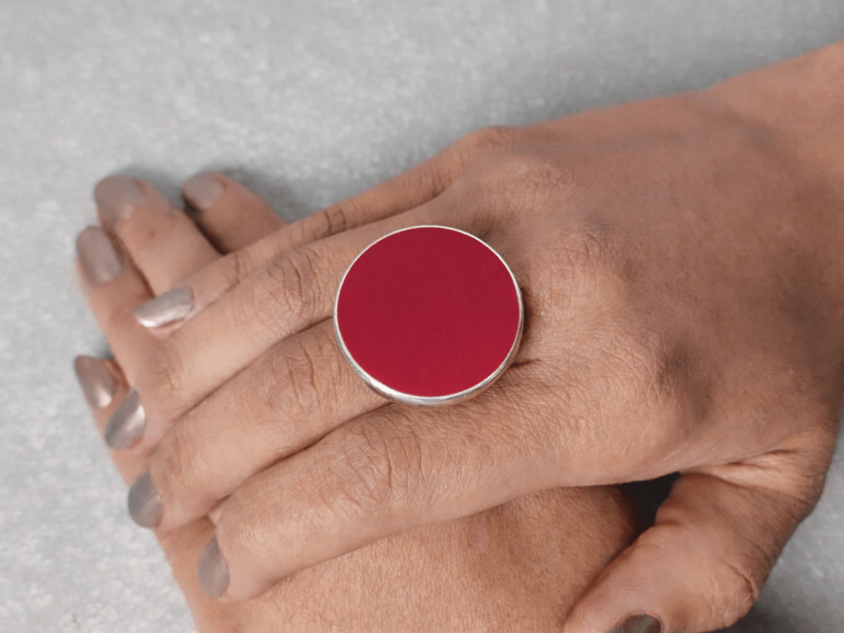 A models hand wearing a round dark red ring