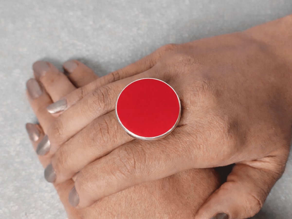 A models hand wearing a round red ring
