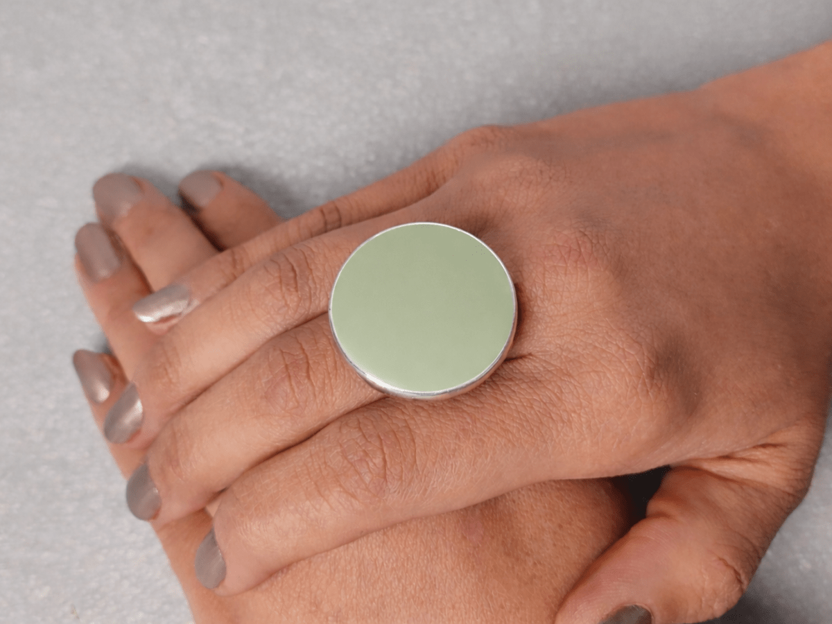 A models hand wearing a round sage green ring