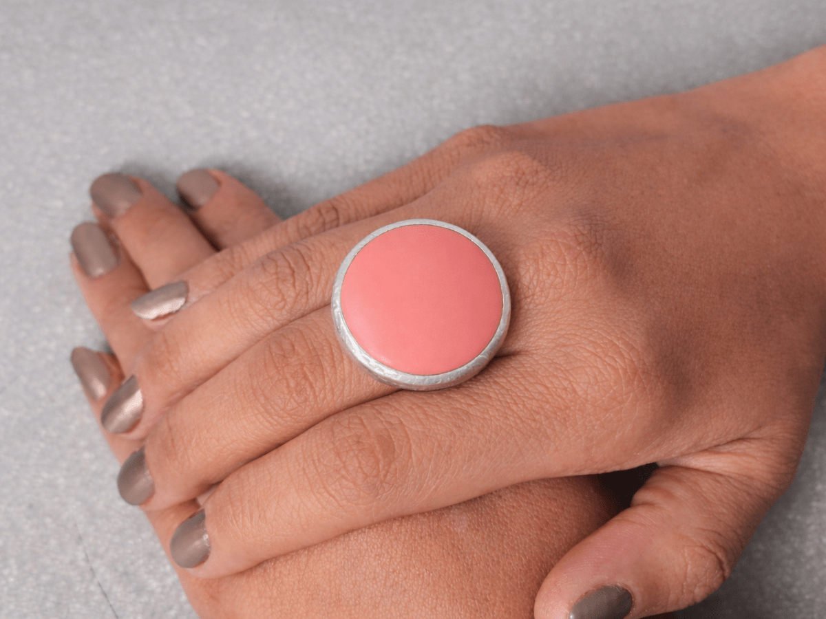 A models hand wearing a round salmon pink ring