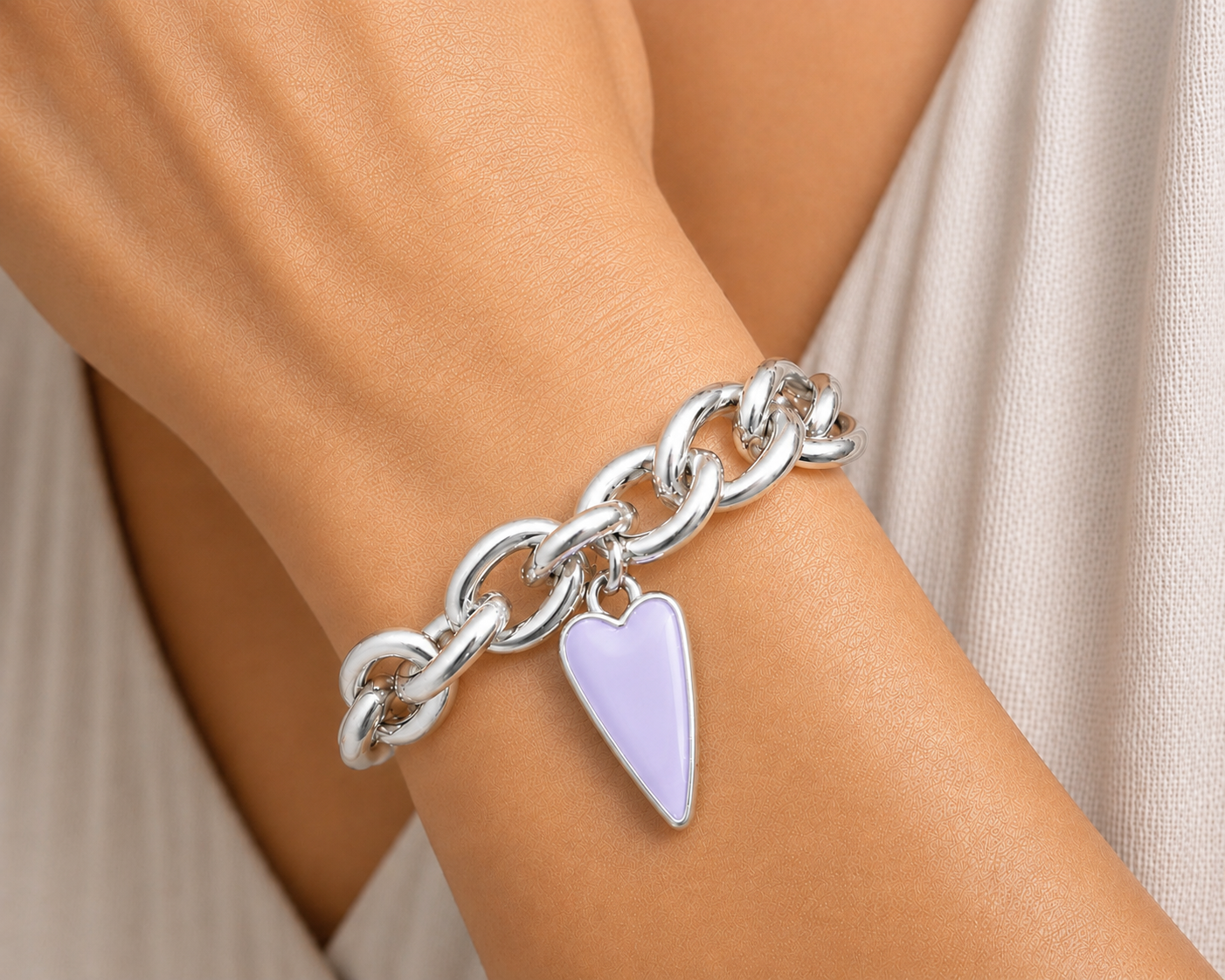 Silver chain bracelet with a heart-shaped purple charm on a wrist.
