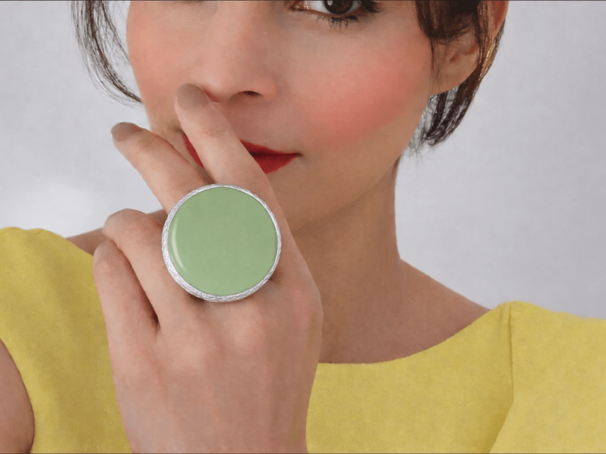 A model wearing a yellow dress and a large sage green ring