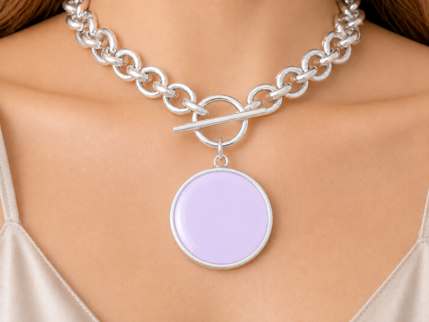 Silver chain necklace with a round purple pendant on a person wearing a beige top. Main image
