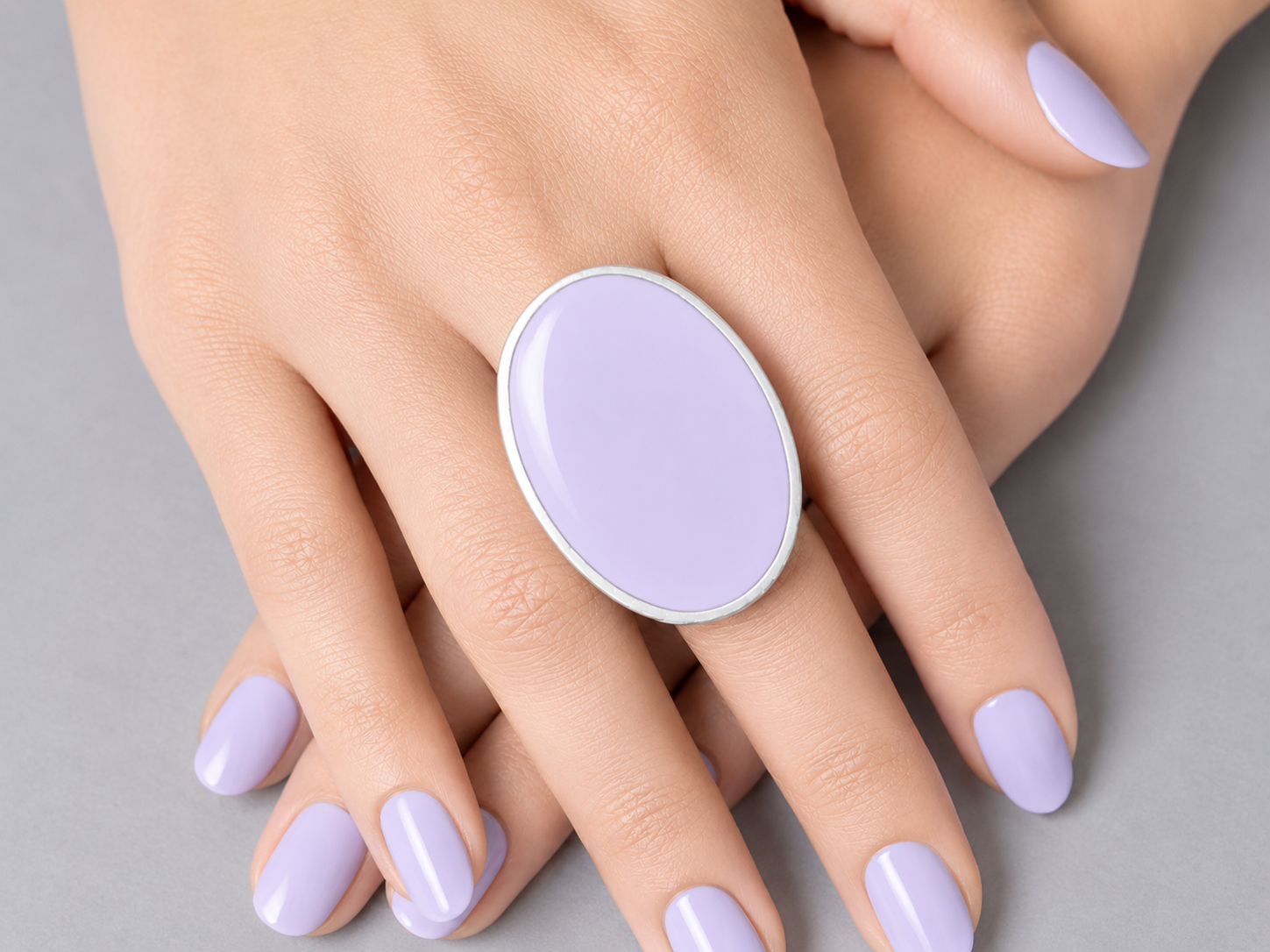 Hand wearing a lavender ring with matching nail polish on a neutral background Main image