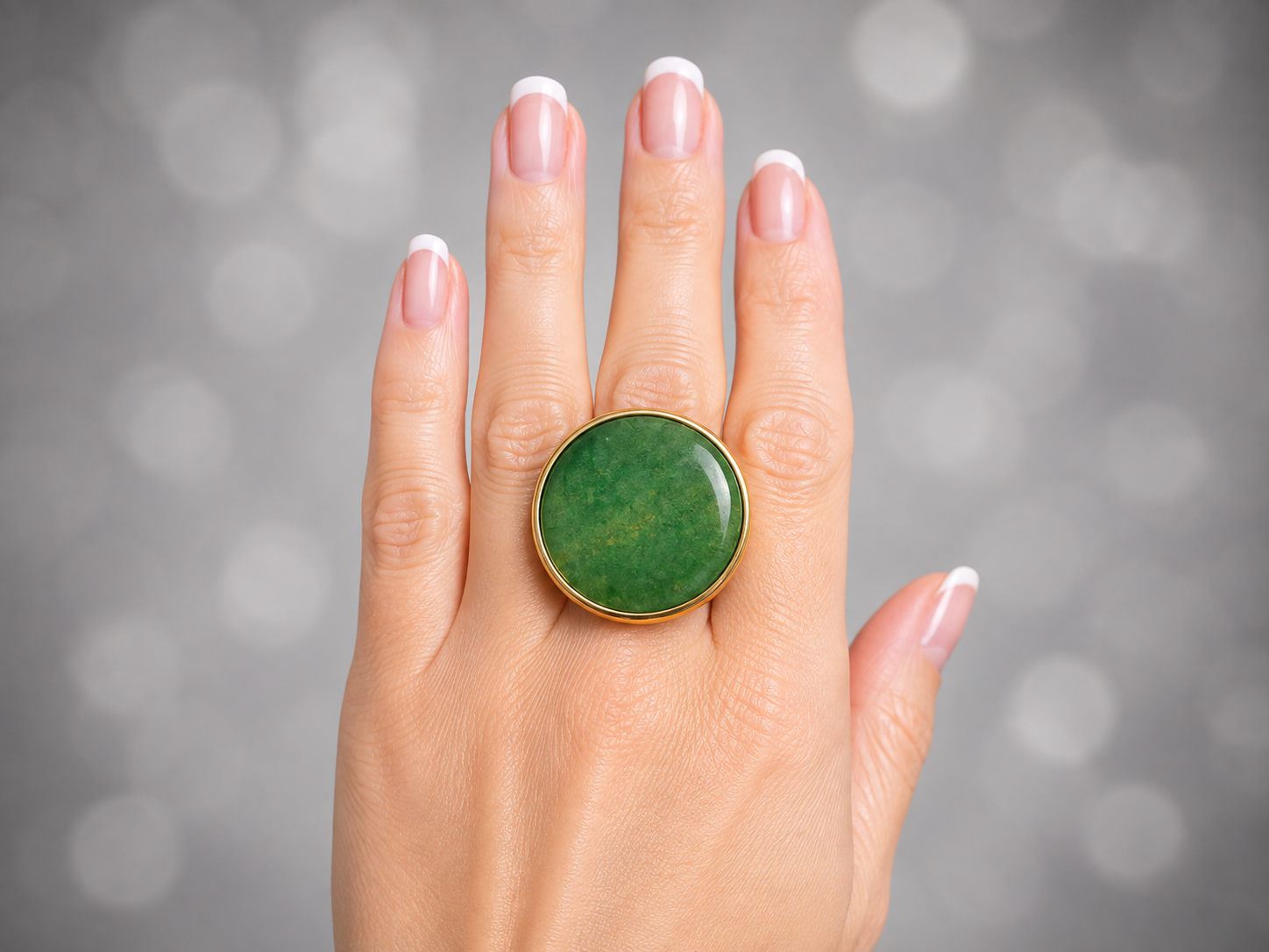 a close up of a models hand wearing a green Aventurine round ring against a grey background