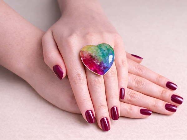 Hand wearing a colorful heart-shaped ring on a light background