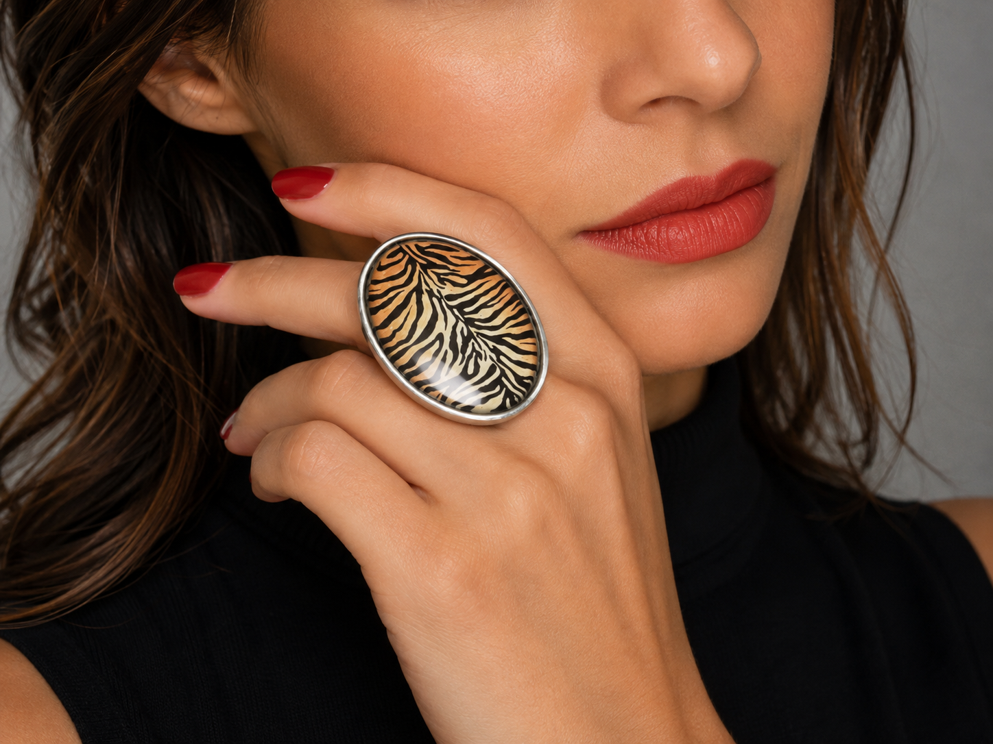 A close-up lifestyle shot of a model wearing a large oval silver ring with a black and orange tiger-stripe pattern on the finger.