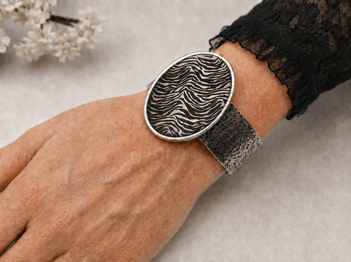 A close-up of a person's wrist wearing a wide silver cuff bracelet with a large oval face featuring a black and white zebra-stripe pattern.