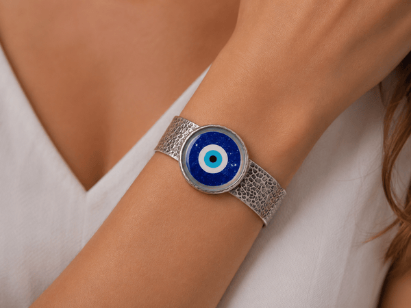 A wise silver cuff bracelet with an evil eye center piece being worn on a models arm