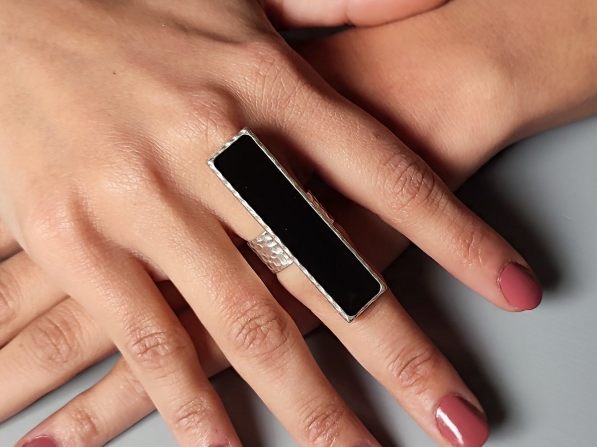 A models hand wearing a long narrow black ring with silver band