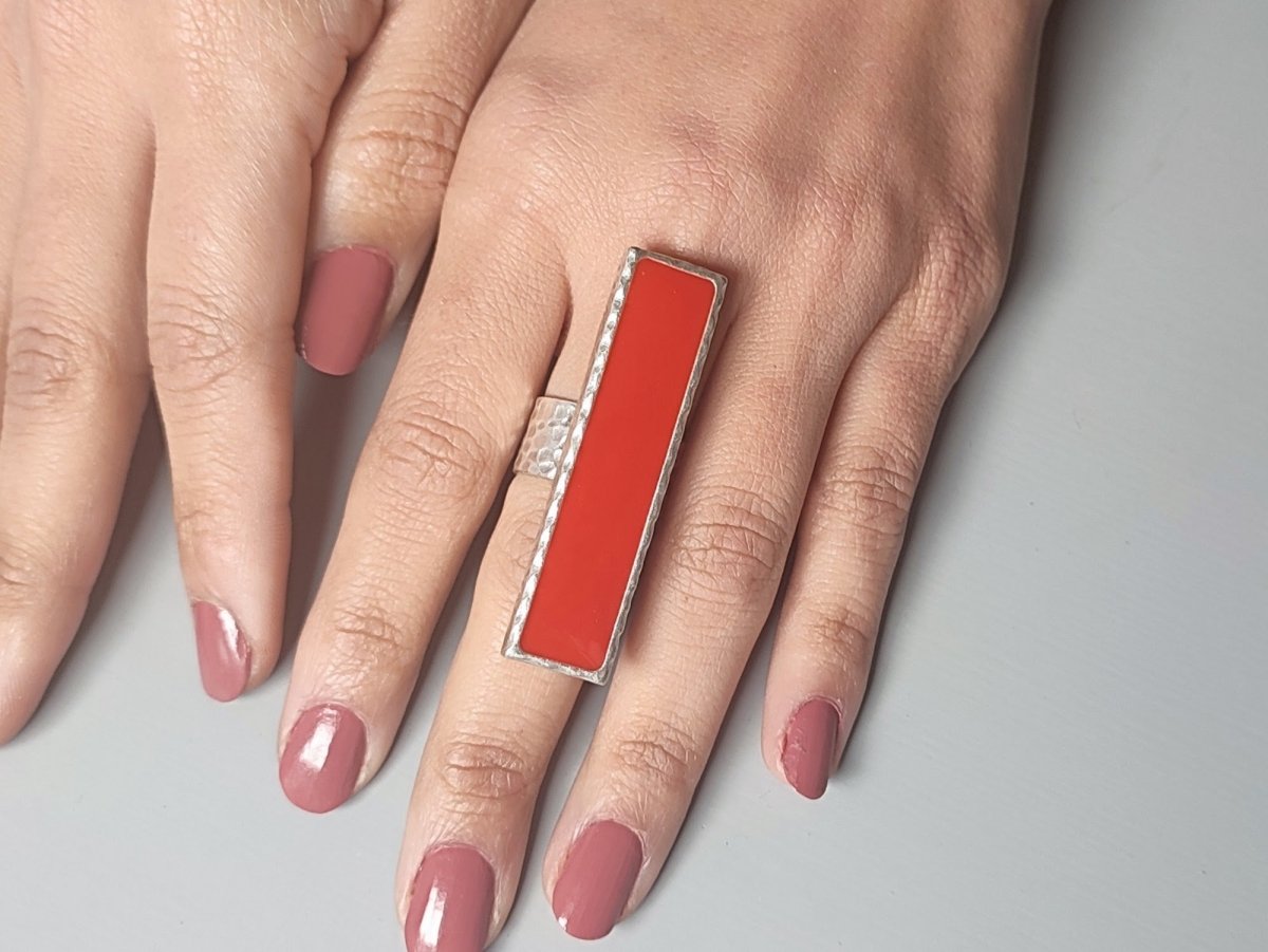 A models hand wearing a long narrow red ring with silver band