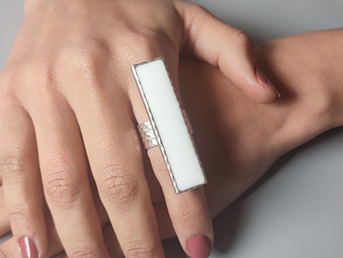 A models hand wearing a long narrow white ring with silver band