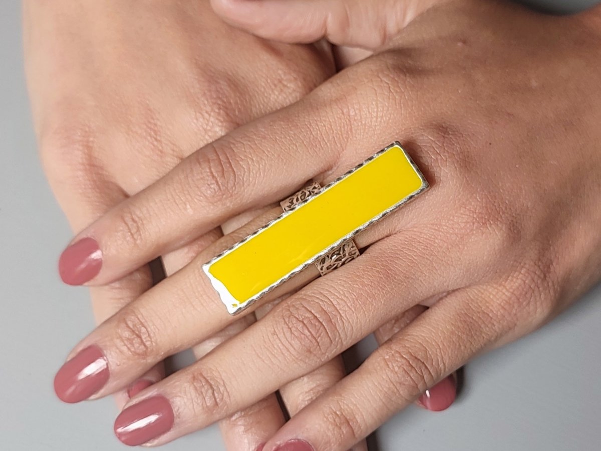 A models hand wearing a long narrow yellow ring with silver band