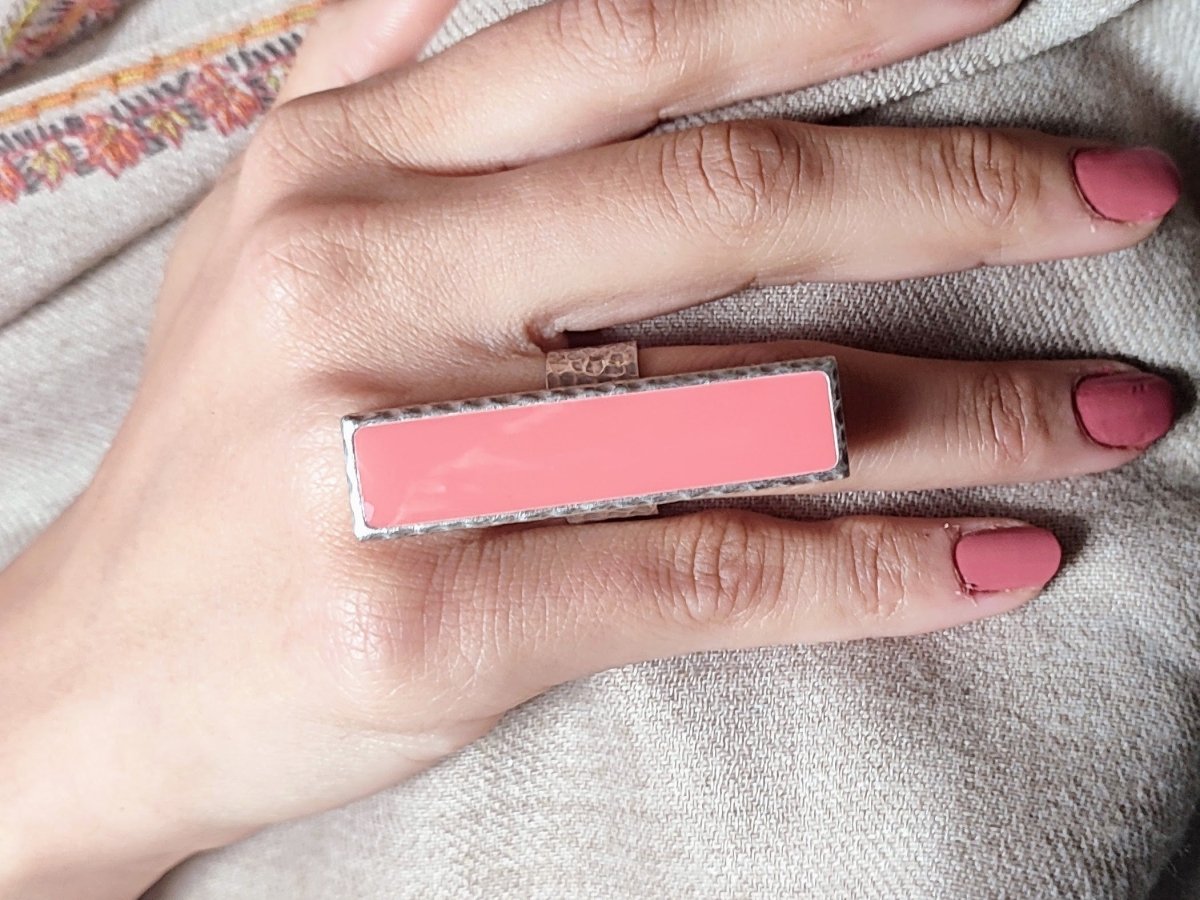 A models hand wearing a long narrow salmon pink ring with silver band
