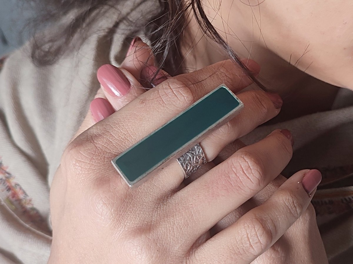 A models hand wearing a long slim dark green ring Main image