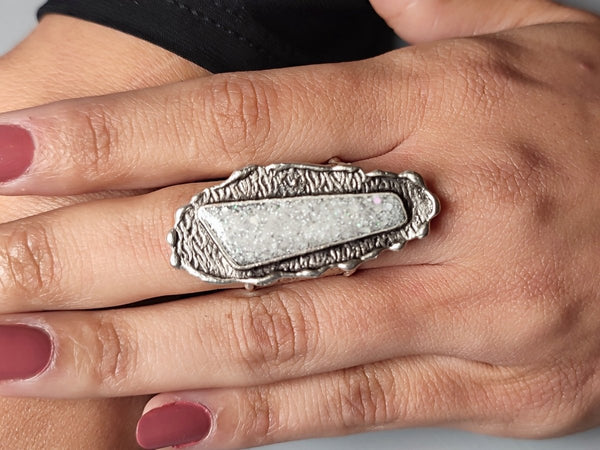 a decorative white glitter statement ring worn on a models hand