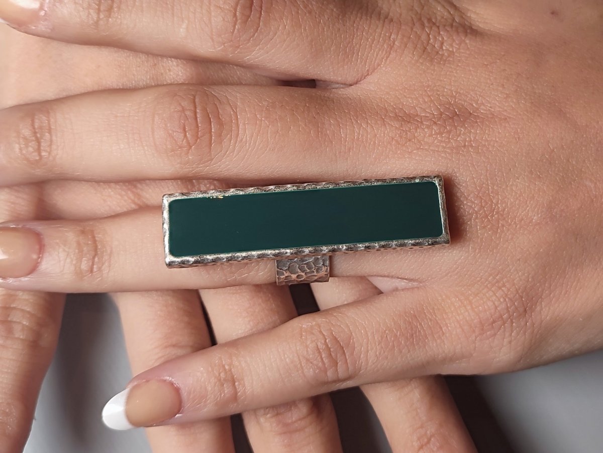 A models hand wearing a long narrow dark green ring with silver band
