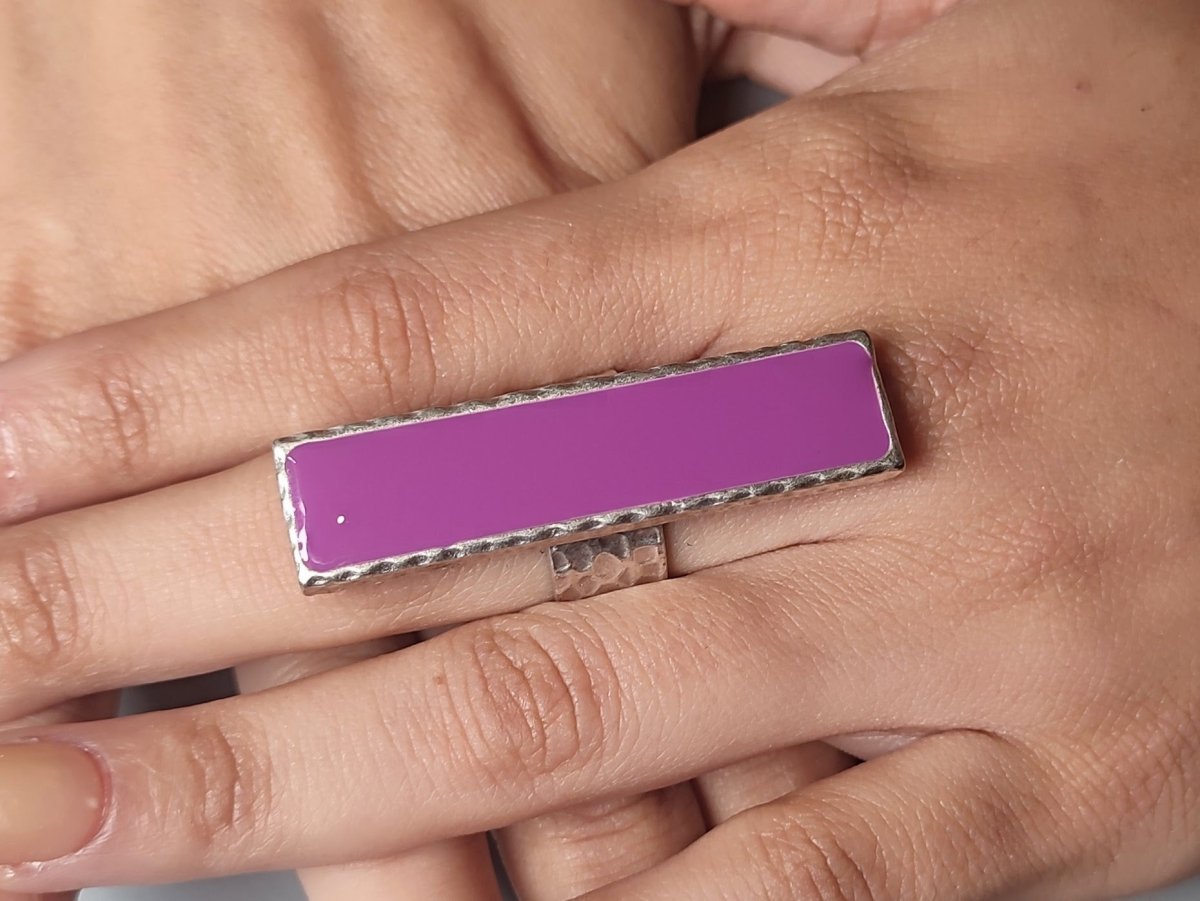 A models hand wearing a long narrow violet ring with silver band