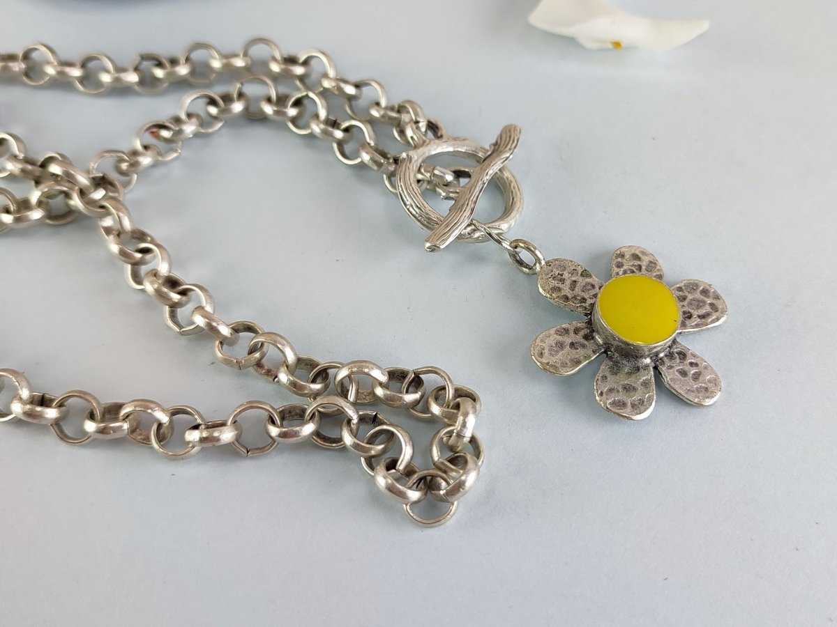 A silver daisy with yellow centre suspended from a silver chain