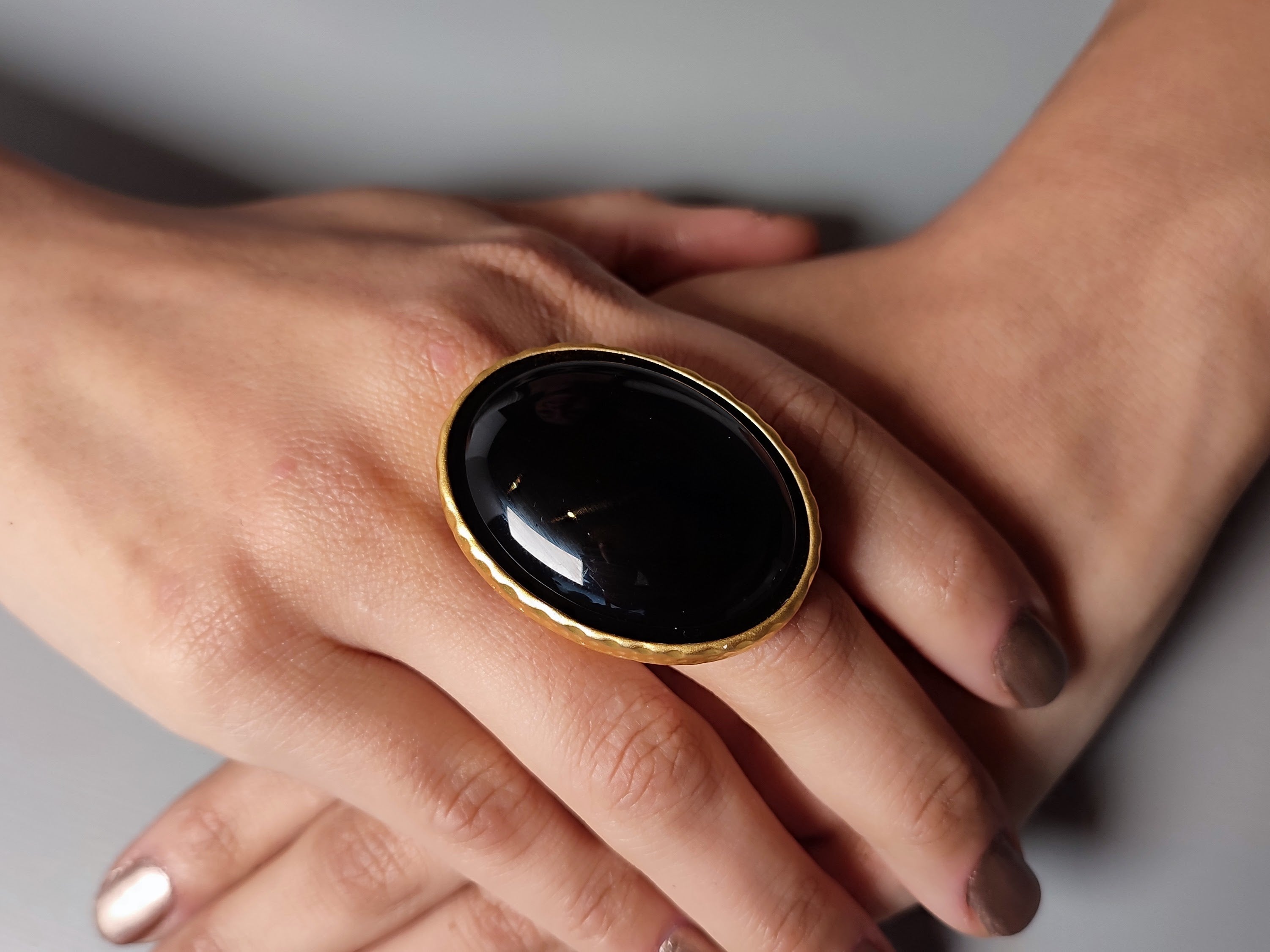 An oversized oval ring with black onyx and gold design, worn on a person's finger. Main image
