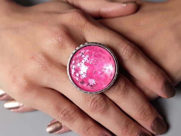 a round pink glitter cocktail ring worn on a models hand