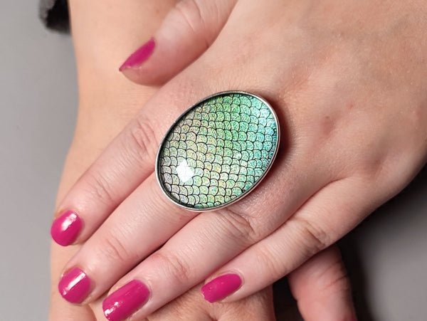 a model wearing a large green oval ring with a mermaid scale pattern