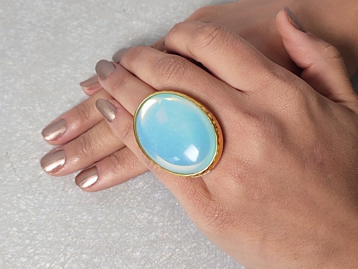 A person wearing a large blue stone ring with gold detailing on their finger. Main image