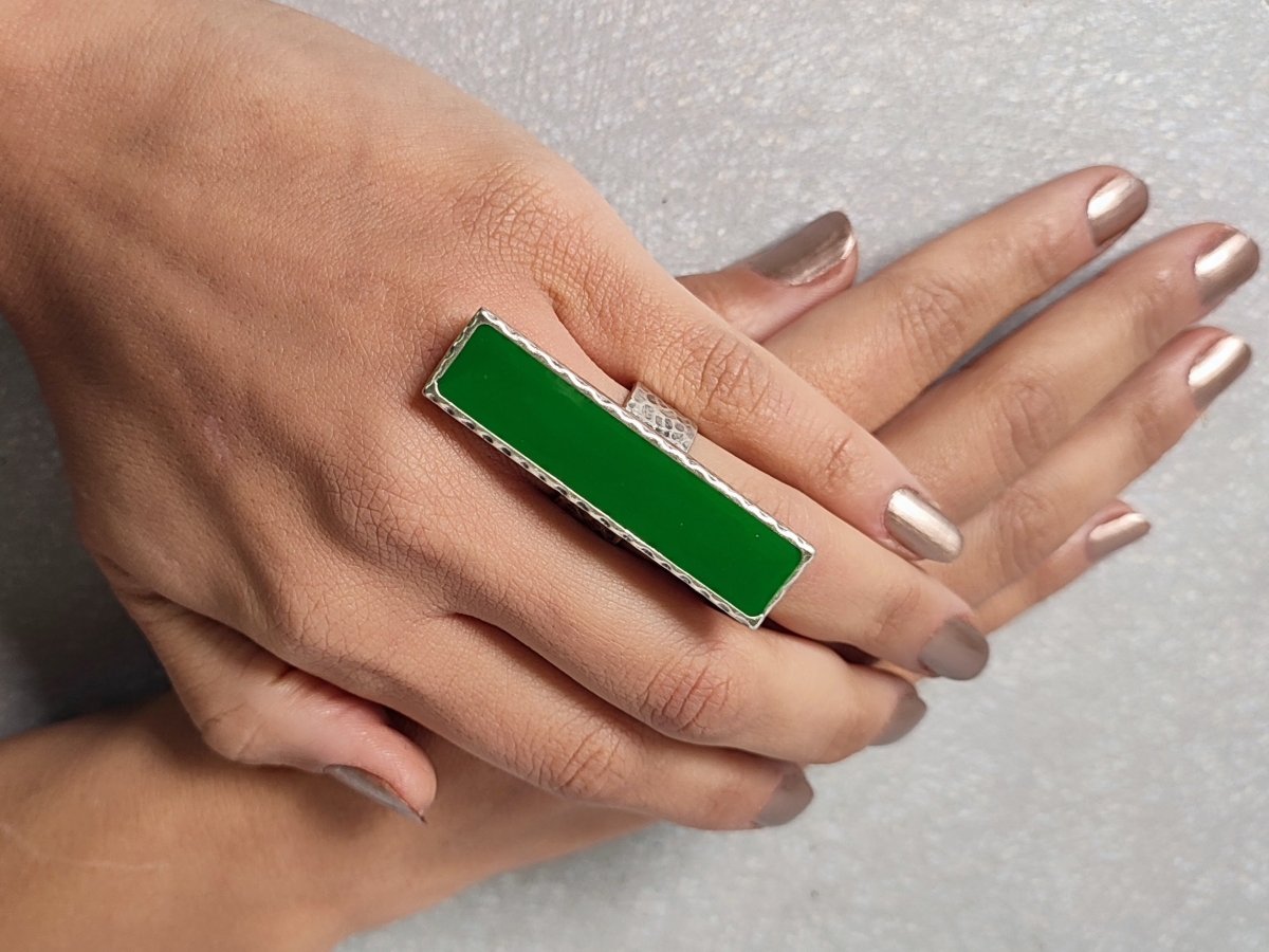 A models hand wearing a long narrow green ring with silver band