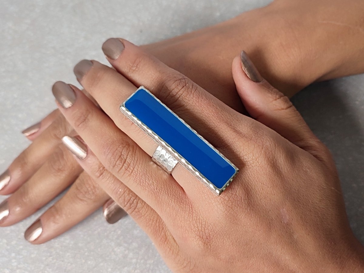 A models hand wearing a long narrow blue ring with silver band Main image
