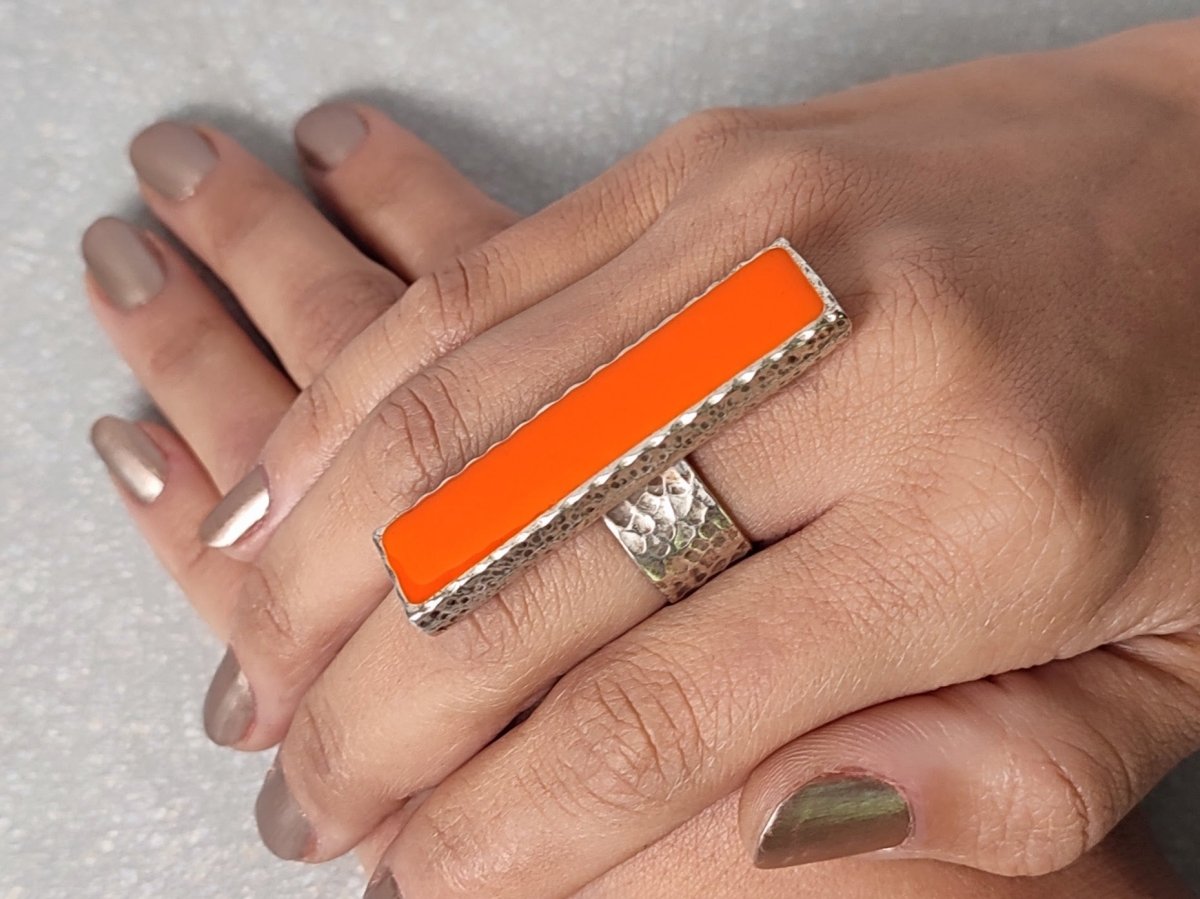 A models hand wearing a long narrow orange ring with silver band