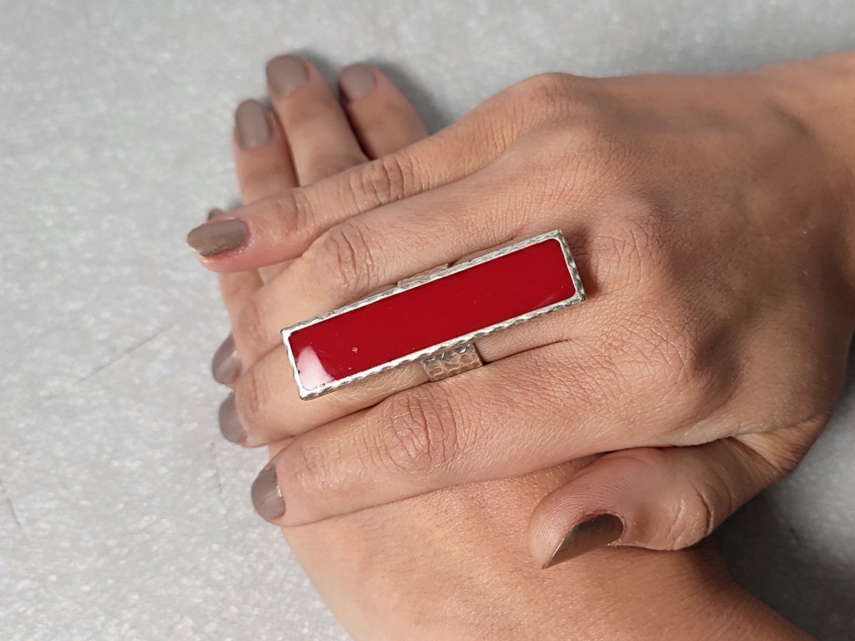 A models hand wearing a long narrow dark red ring with silver band