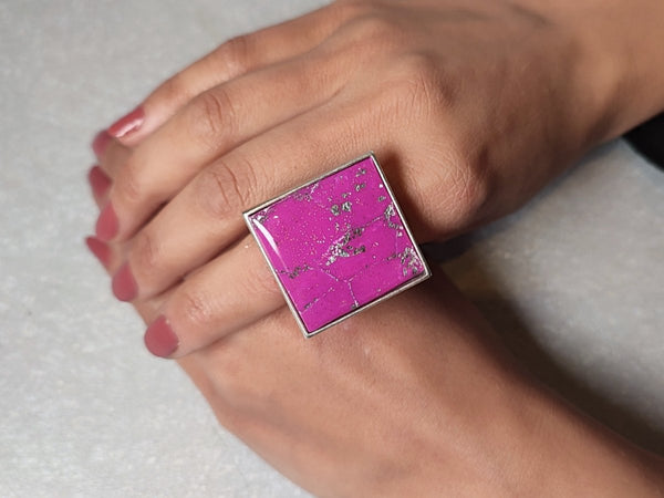 a large square statement ring in pink with flecks of silver worn on a models hand