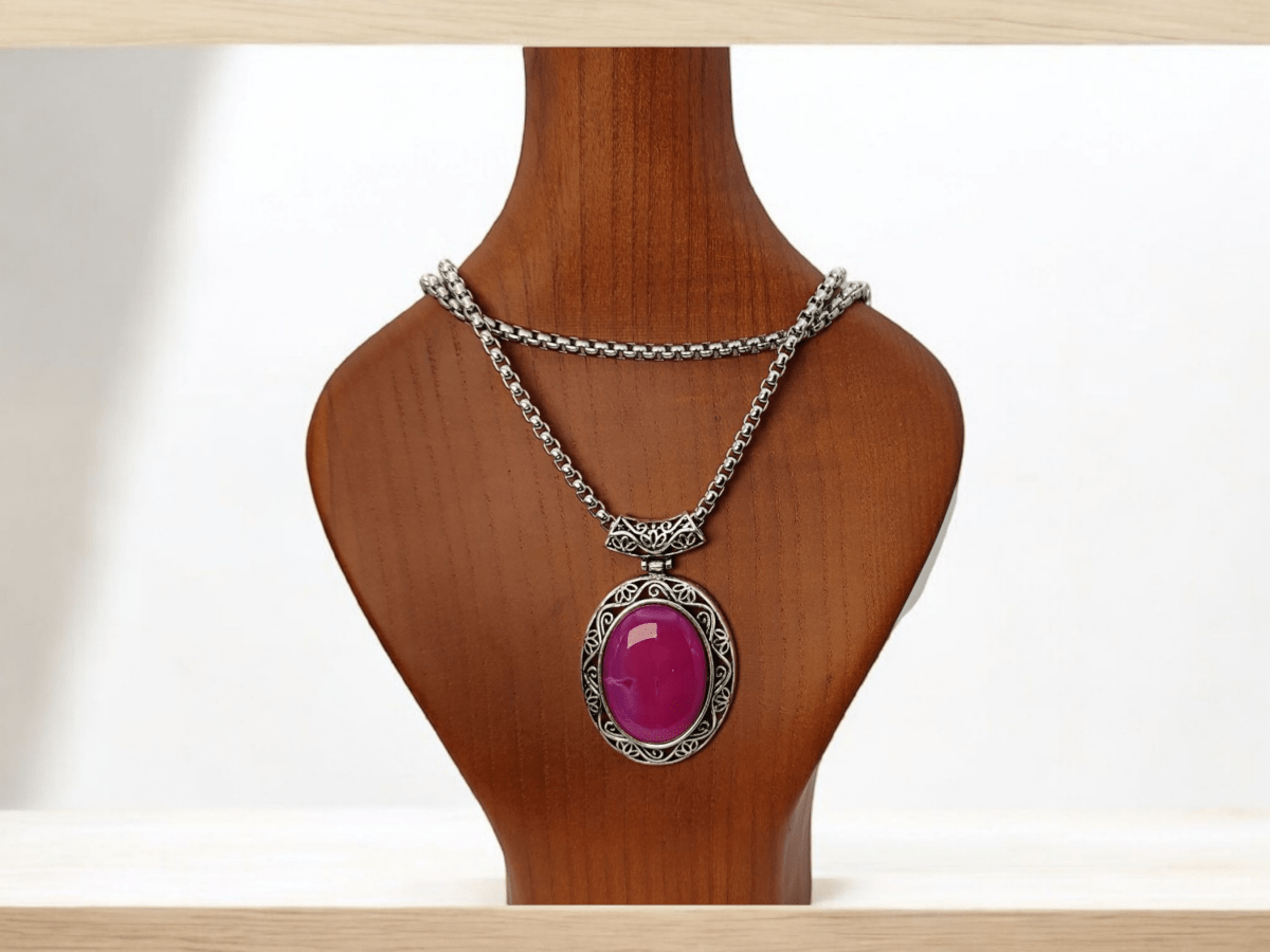 A layered pendant necklace on a silver chain with a pink  centre worn on a wooden bust