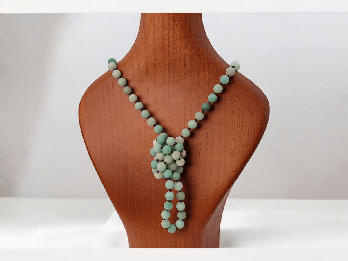 an amazonite beaded necklace tied in a knot on a wooden bust Main image
