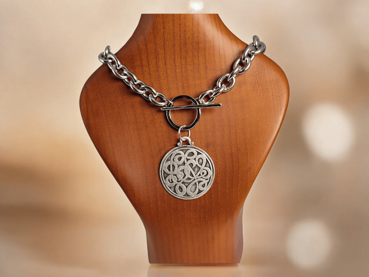 A large silver pendant on a stainless steel chain on a wooden bust Main image
