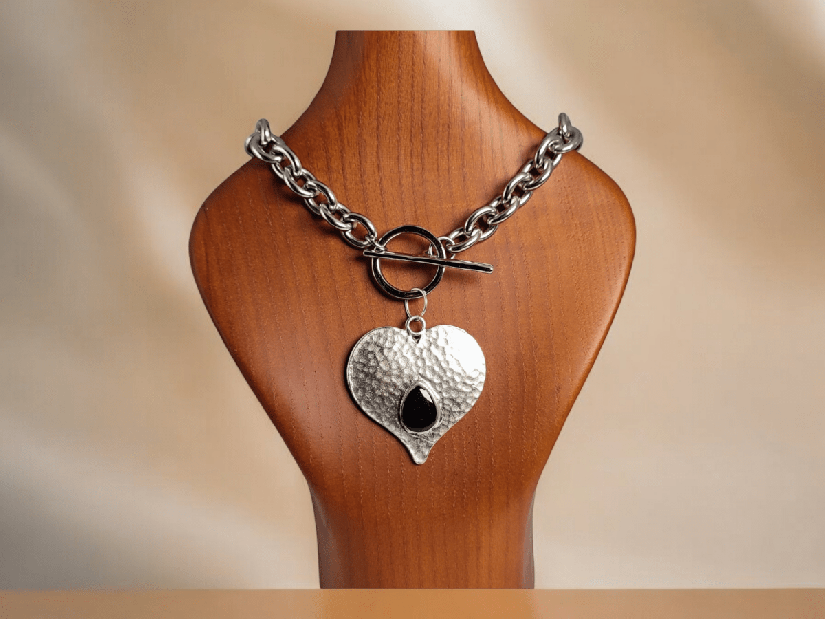 A large heart pendant with black detail and a chunky chain on a wooden bust Main image