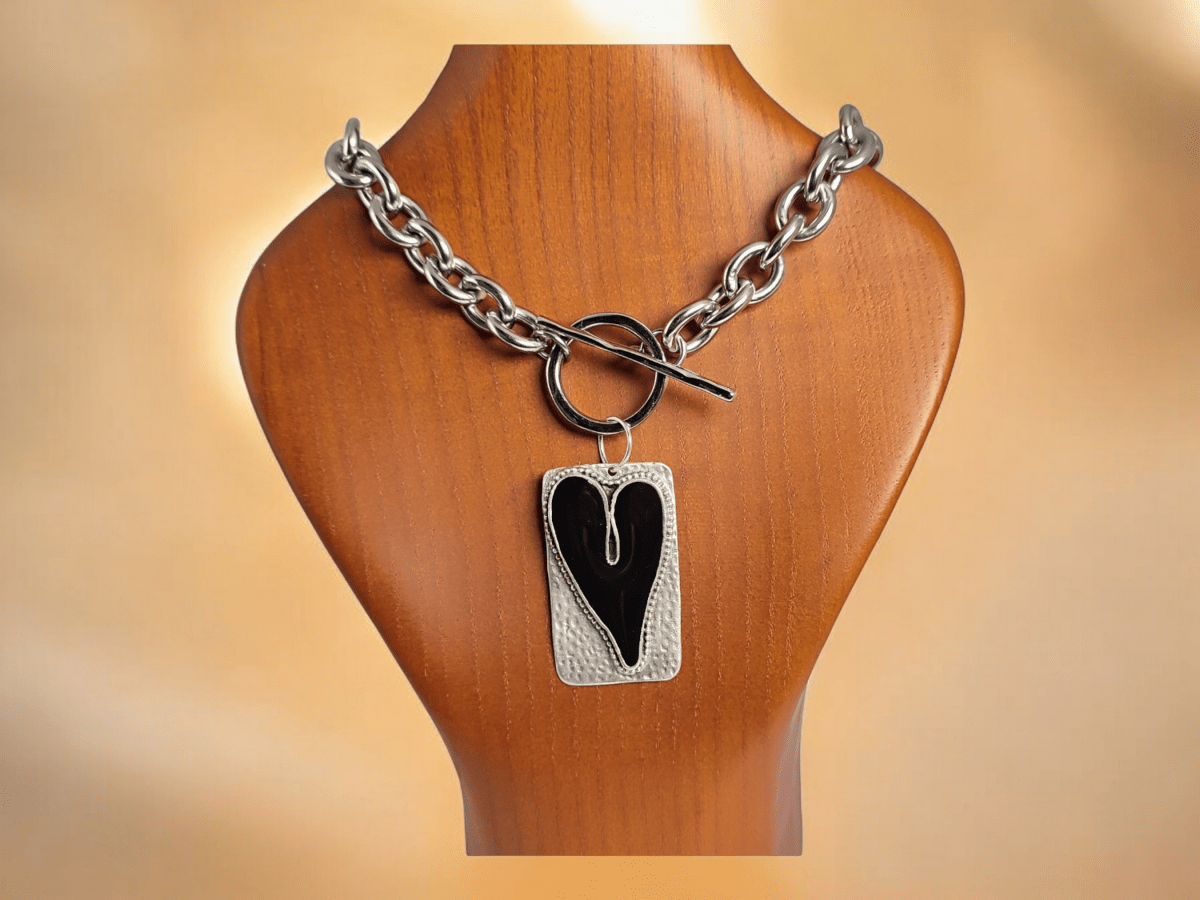 A rectangular pendant with a black heart centre suspended from a chunky chain on a wooden bust