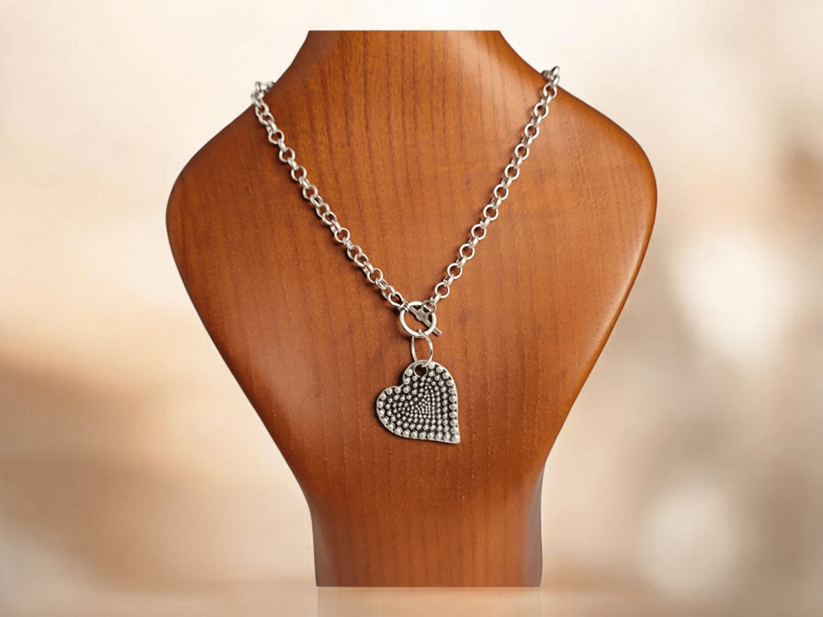 A silver heart suspended from a silver chain on a wooden bust