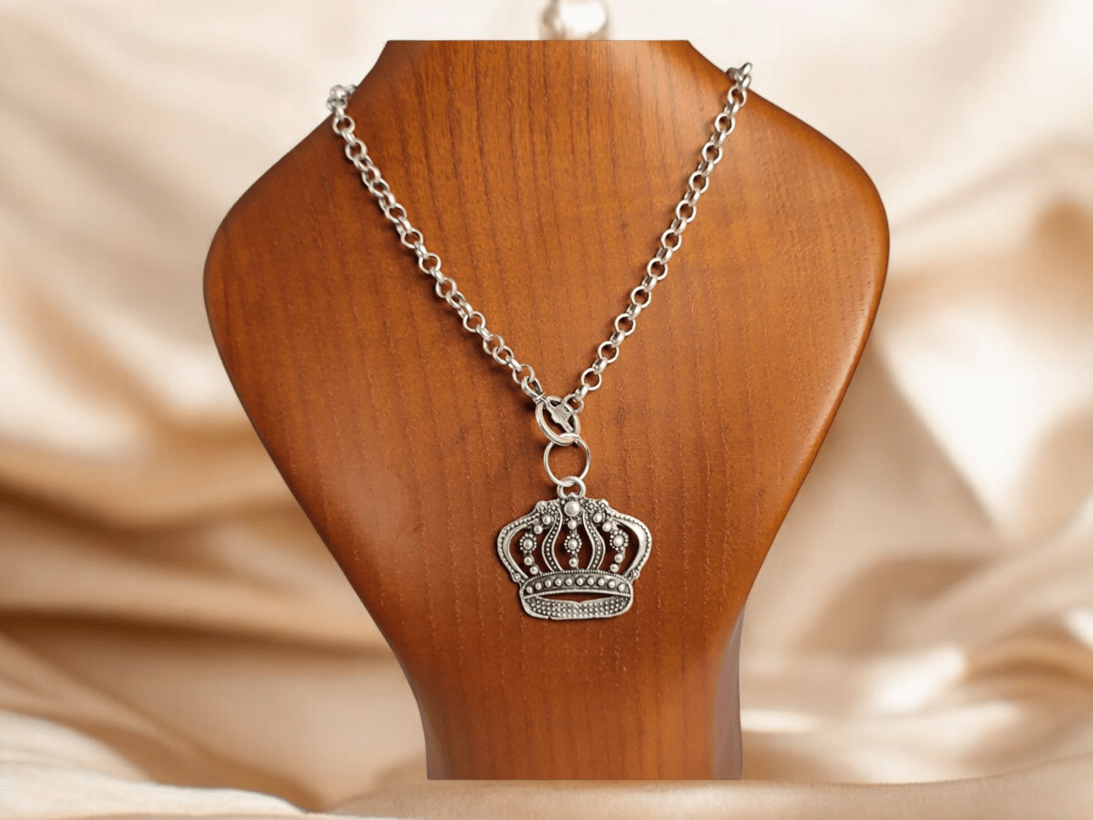 A silver crown charm suspended from a silver chain on a wooden bust Main image