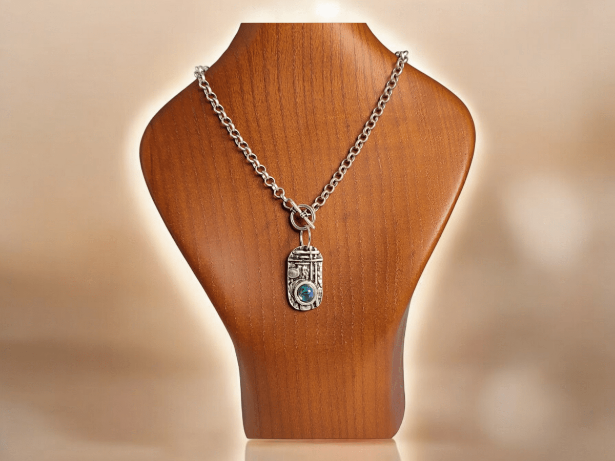 A silver pendant with blue stone worn on a wooden bust Main image