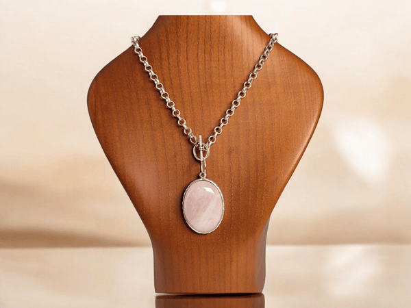 A pink rose quartz pendant on a wooden bust