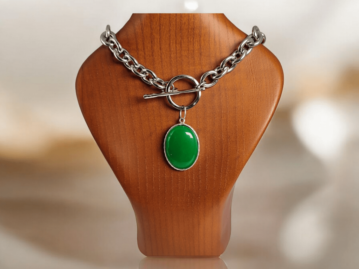 A Jade pendant on a stainless steel chain on a wooden bust Main image