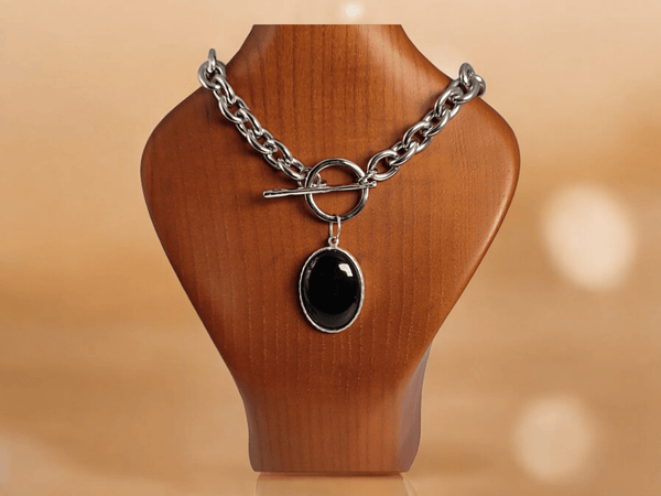 A black onyx pendant on a stainless steel chain on a wooden bust