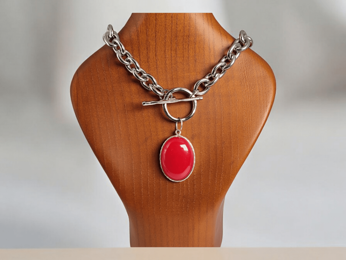 A red Jade pendant suspended from a chunky silver chain on a wooden bust Main image