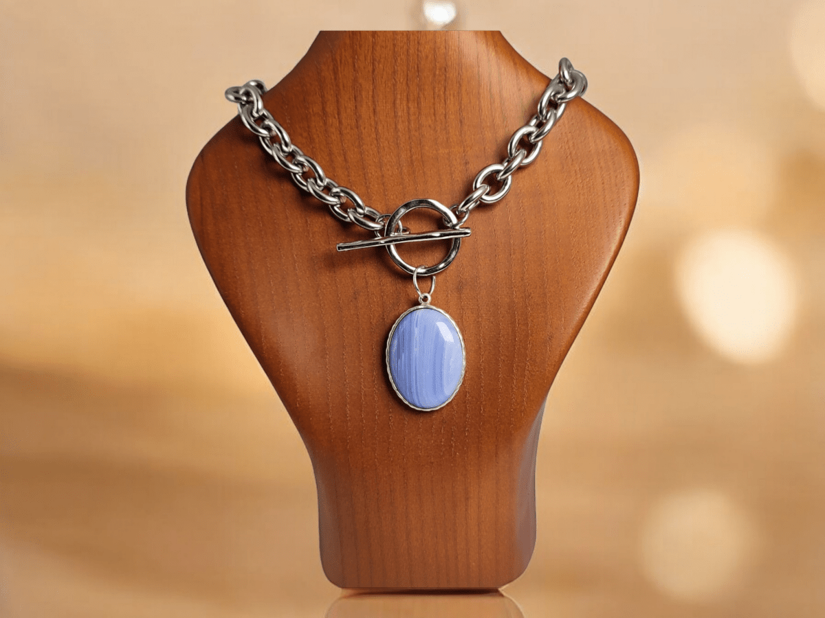 A blue stone pendant suspended from a chunky stainless steel chain worn on a wooden bust
